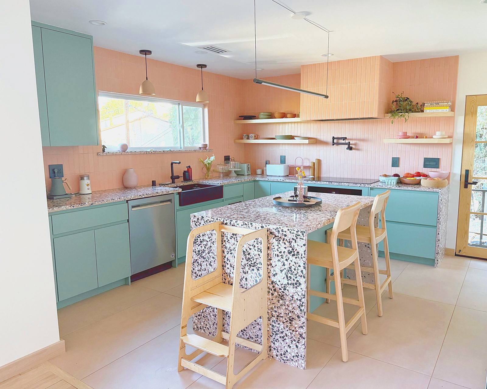 Pink and sage kitchen with terrazzo island, oak stools and open shelving