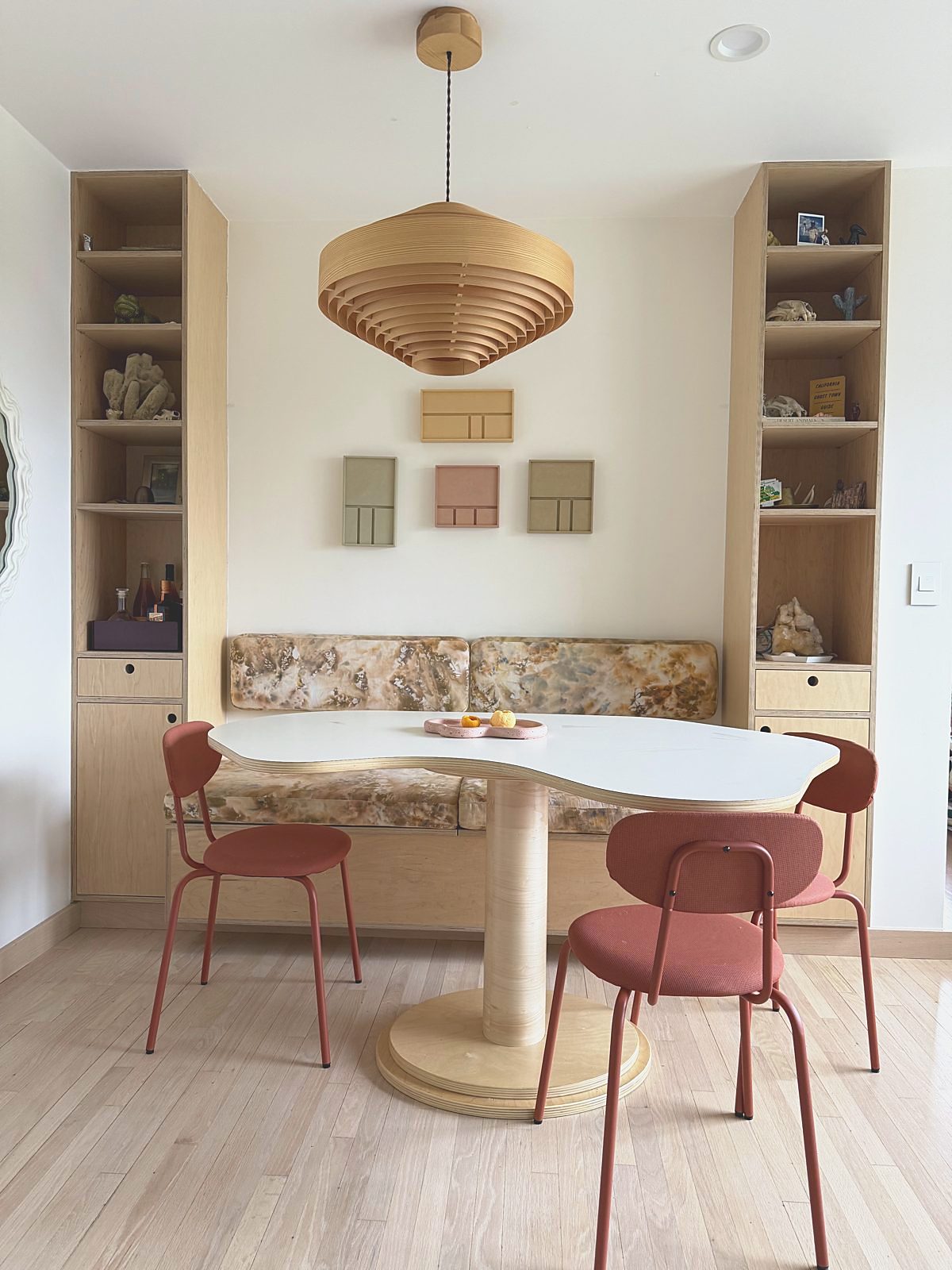 Sunny breakfast nook with an organic white table, rust chairs, oak shelving and a woven pendant