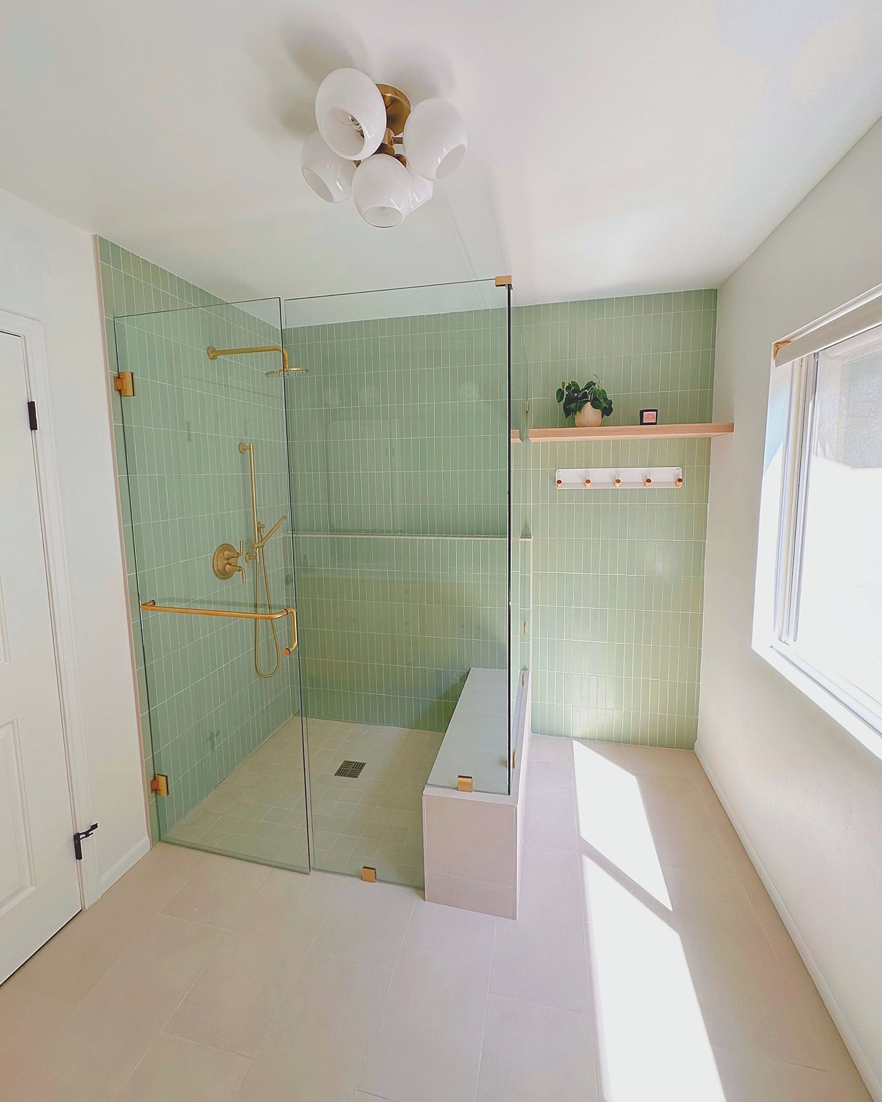 Sage green tiled bathroom with walk-in shower and brass fixtures