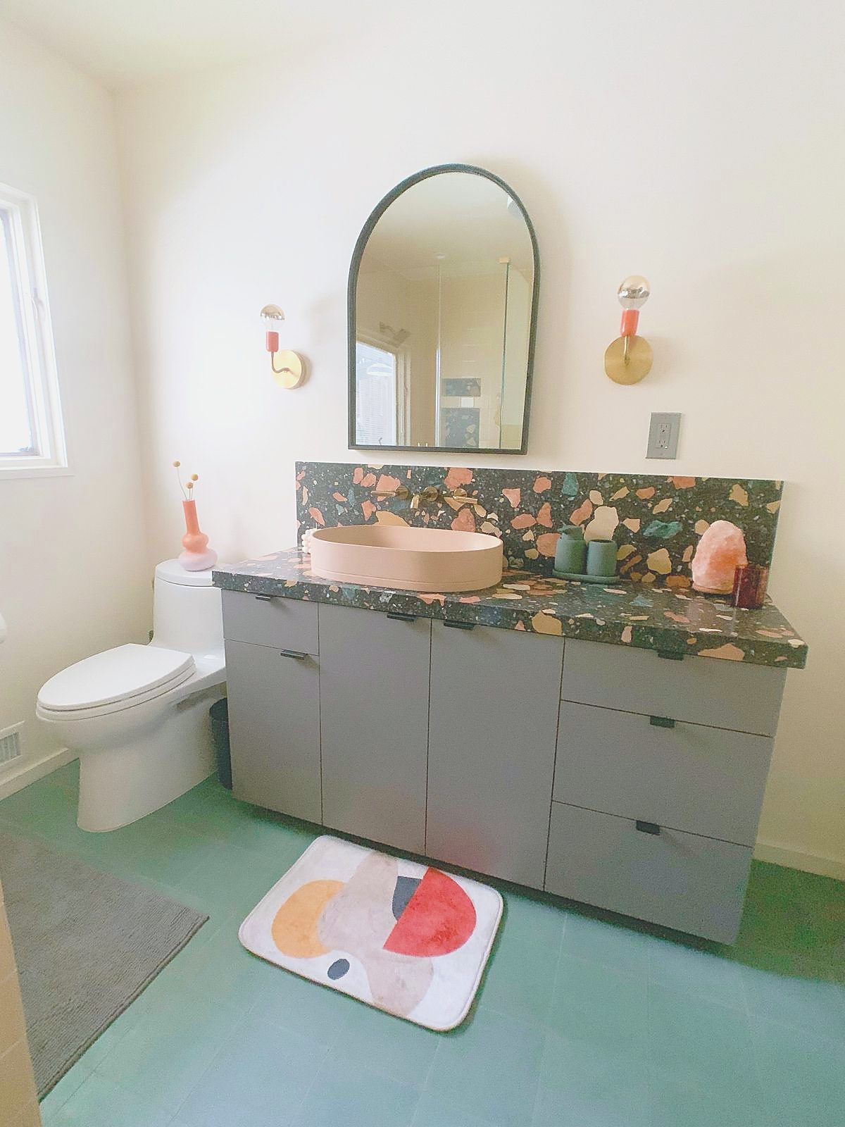 Bathroom with terrazzo vanity top, blush vessel sink and arched mirror